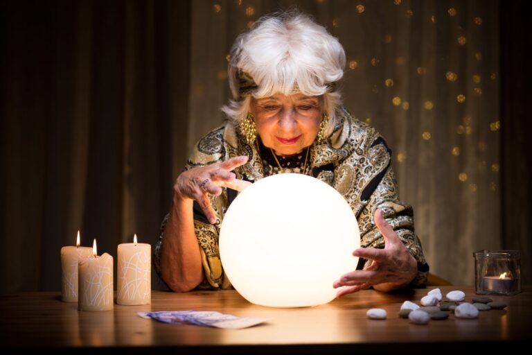 Photograph of an older "fortune teller" figure peering into a crystal ball.