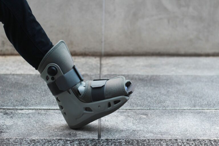 Photograph of a foot in a medical boot, walking on a sidewalk.