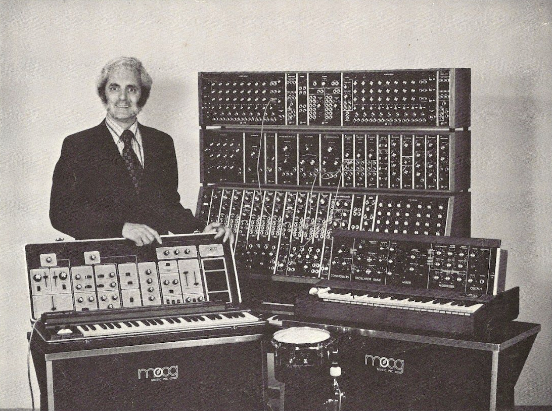 Black and white photo of Bob Moog with his eponymous synthesizers.