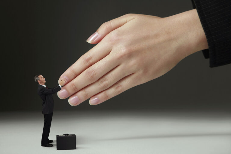 A businessman in a suit with a briefcase at his feet shaking hands with a giant hand.