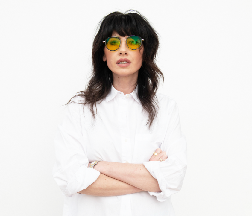 A photograph of Whitney in a white shirt and sunglasses with her arms crossed