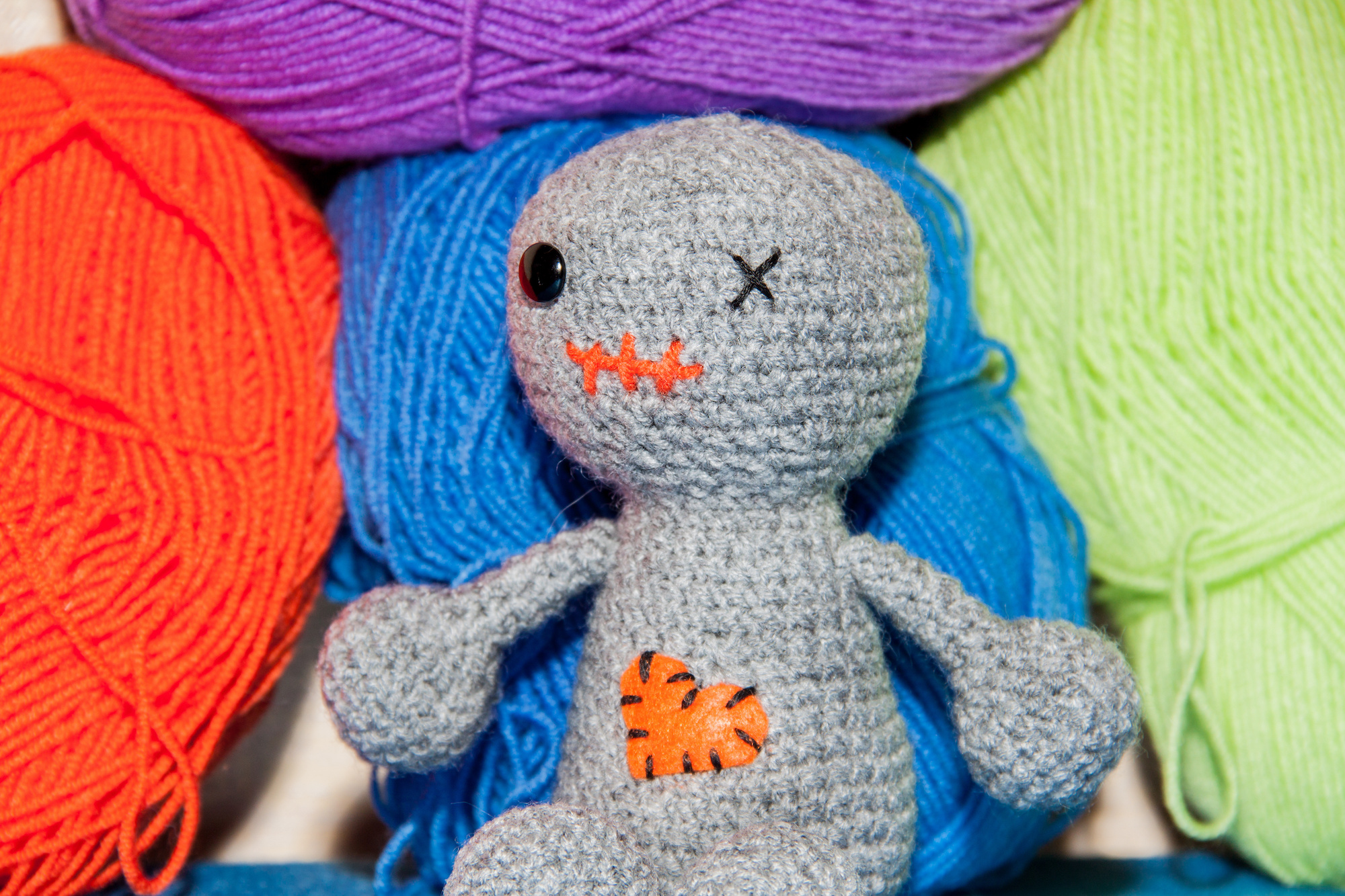 Photograph of a "zombie" knit doll sitting on top of skeins of yarn