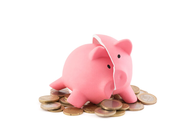 Photograph of a classic pink piggy bank, cracked cleanly in half, sitting on top of a pile of gold coins.