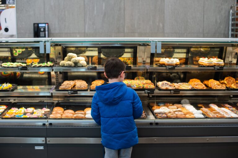 Image of a child standing in front of a large display case of doughnuts.