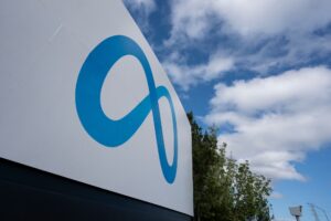 A photograph of the Meta logo on a building with a blue sky and clouds behind it.