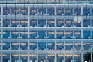 Photograph from the exterior of a large office building with fully glass sides showing many floors of cubicles.