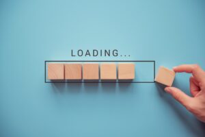 Image of several wooden blocks imitating a loading bar with a hand placing the final block. The word "LOADING" above it. Blue background.