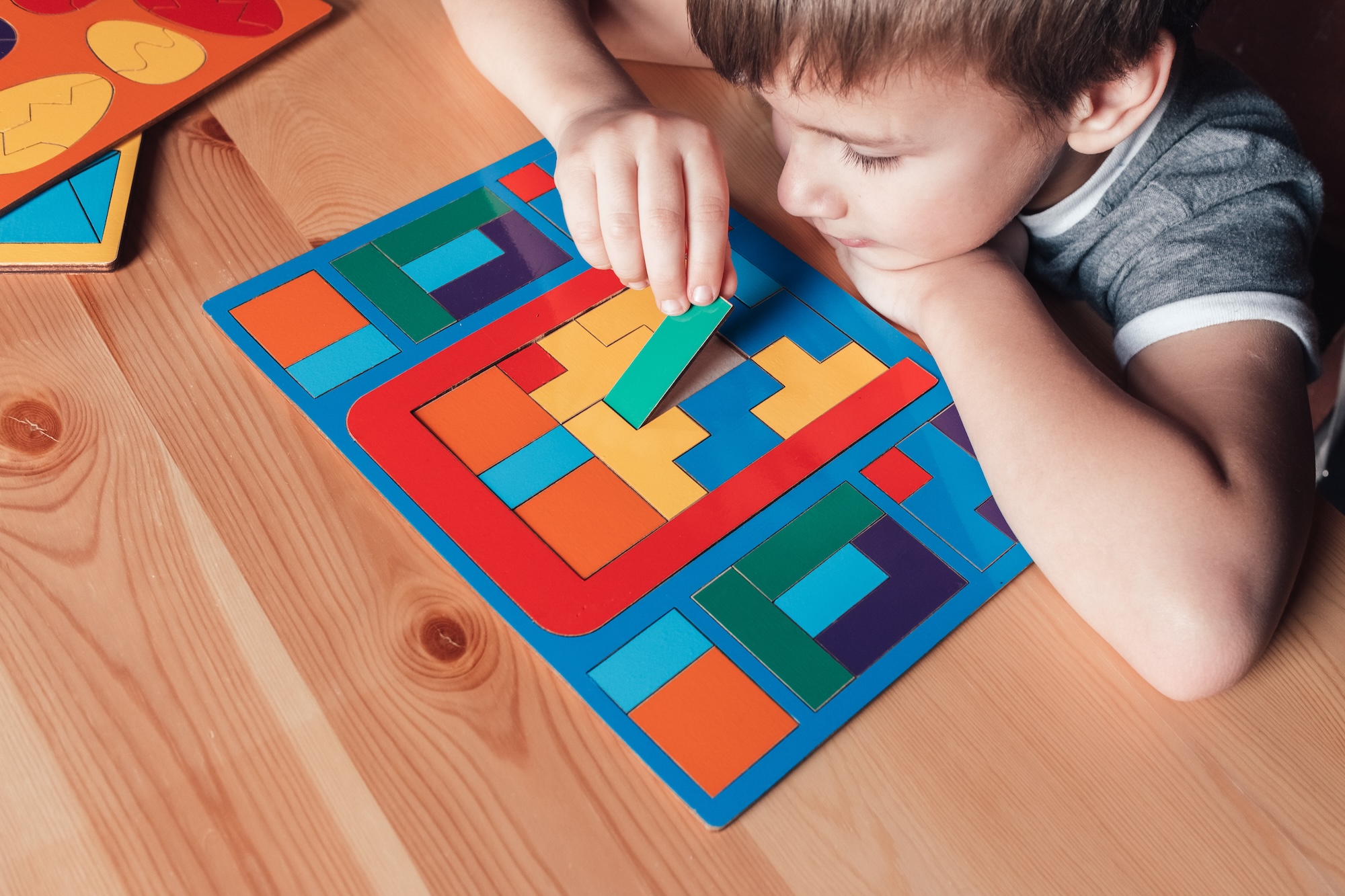 Photograph of a young boy putting a puzzle piece onto a colorful puzzle.