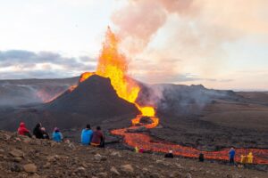 Photograph of an actively erupting volcano, with spectators seated in the foreground.