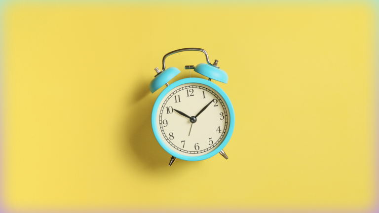 Image of an aqua-colored old-fashioned alarm clock against a yellow background.