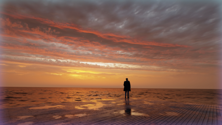 Silhouetted figure at sunset on a beach.