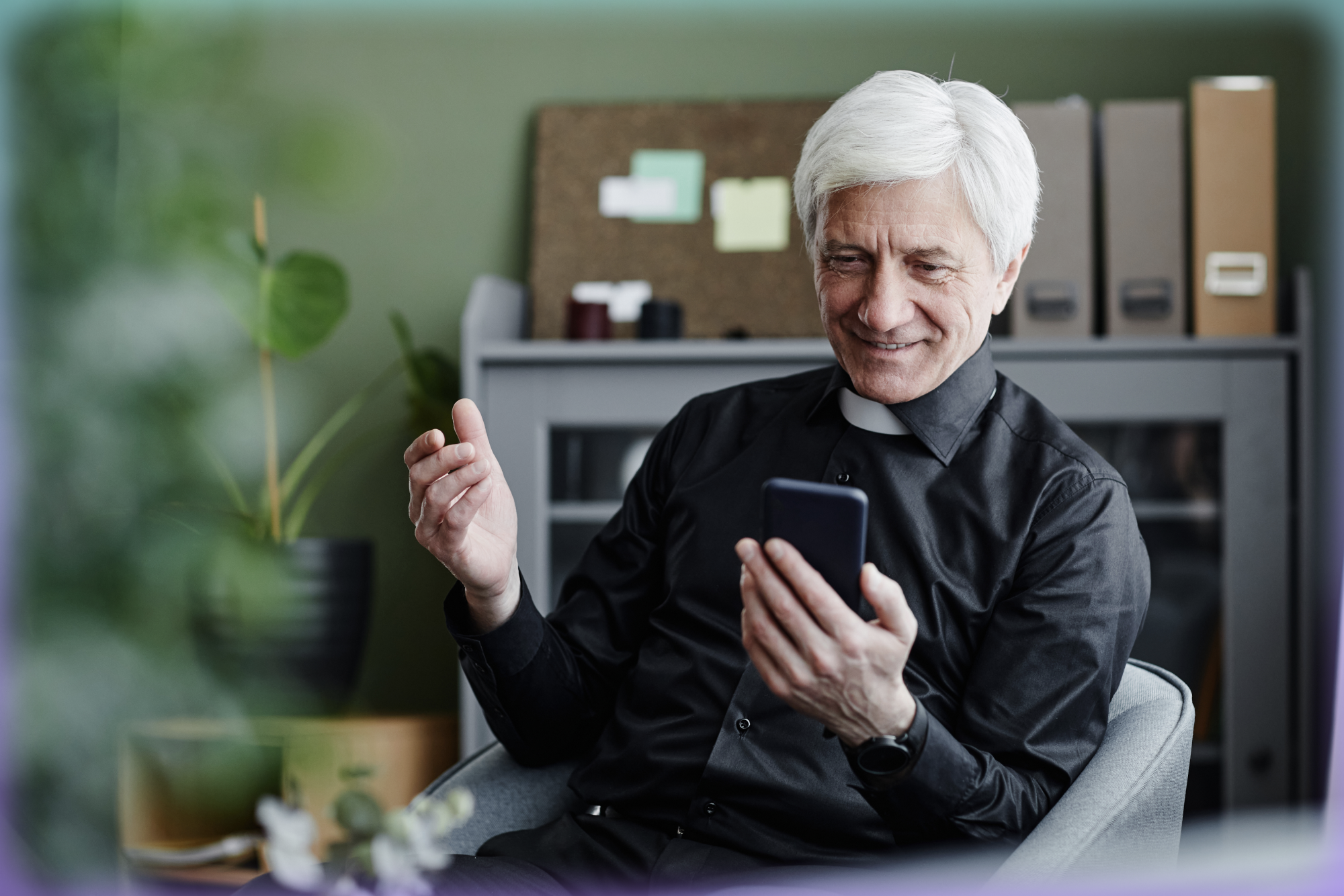 Photograph of a white-haired priest looking at the phone in his hand.