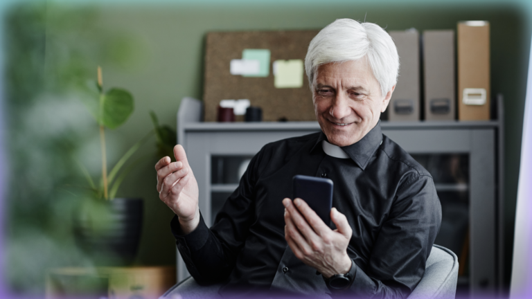 Photograph of a white-haired priest looking at the phone in his hand.