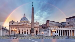 Photograph of St Peter's Square in Vatican City, with a rainbow arcing over St. Peter's Basilica