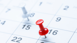 Close-up image of a white and a red push-pin on different calendar dates.