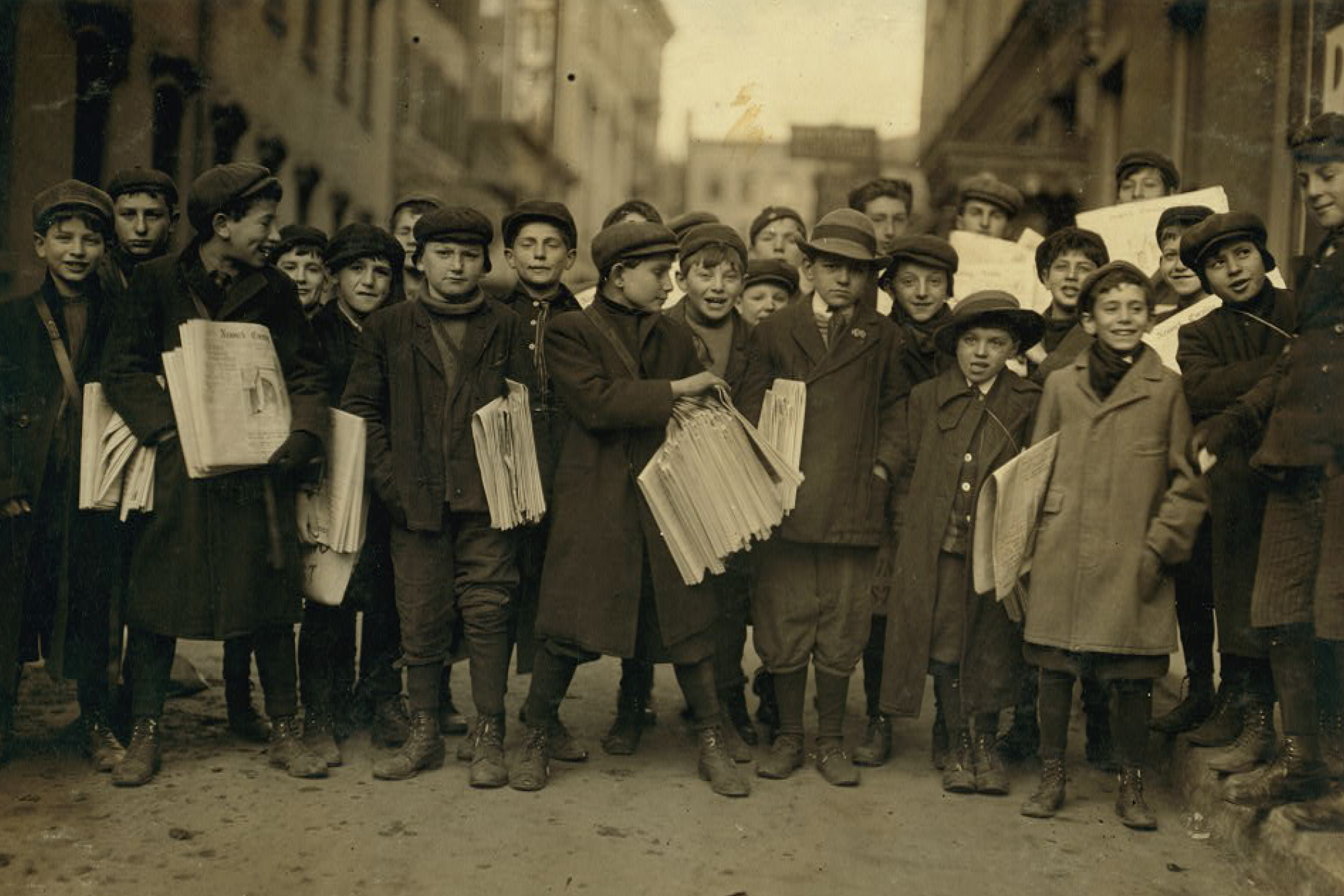 Old photograph in sepia tones featuring a collection of child newspaper sellers.
