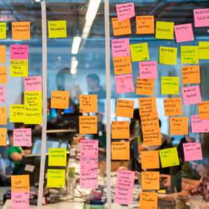 Photograph of a glass wall with many multicolored post-its attached in rows.