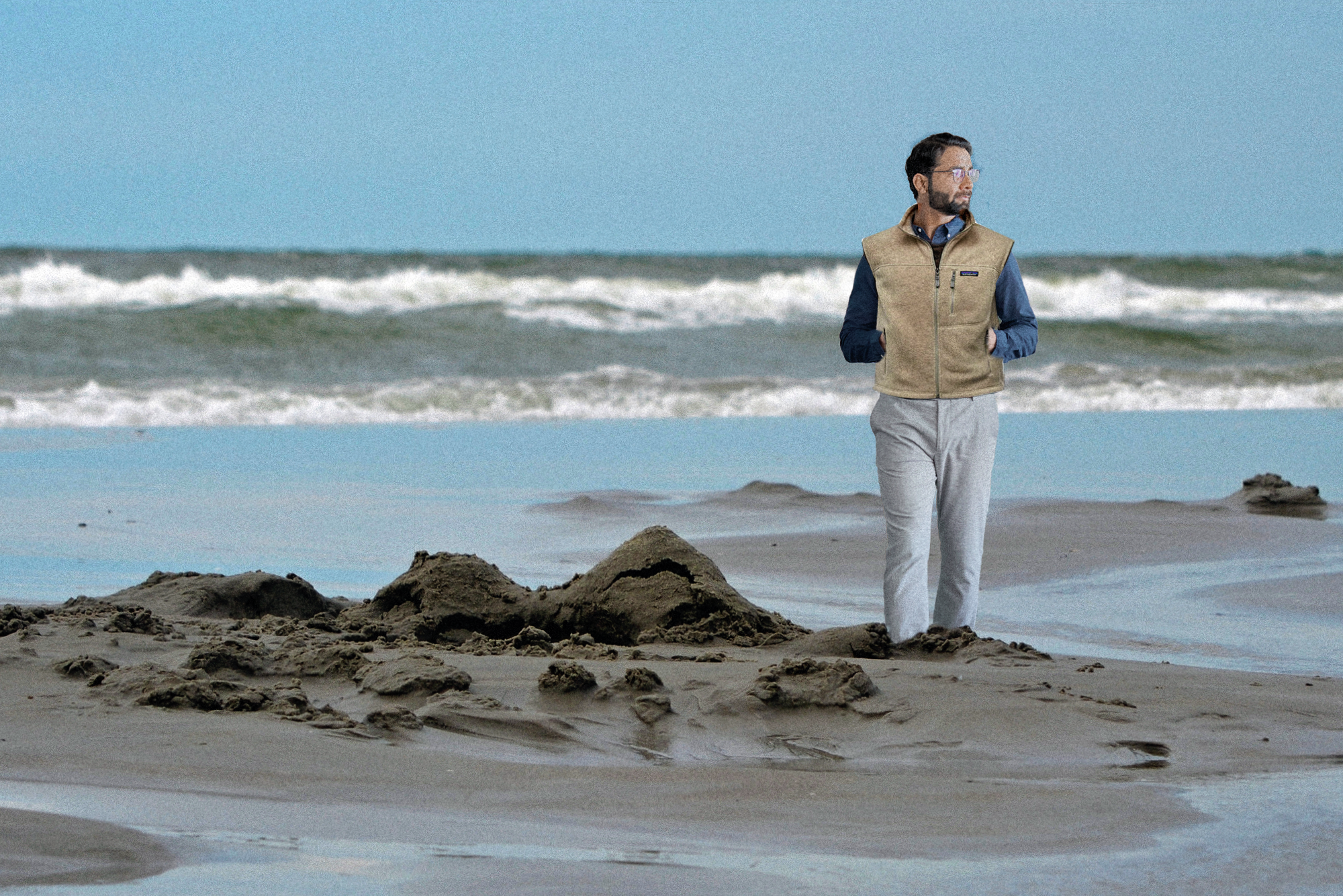 Image of a businessman standing beside a sandcastle on a beach.