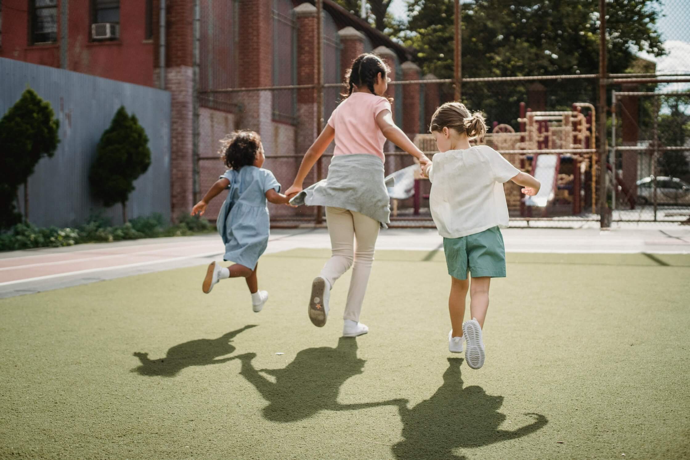 Children running together on a green playground, representing the health outcomes supported by Make an Impact's analytics network