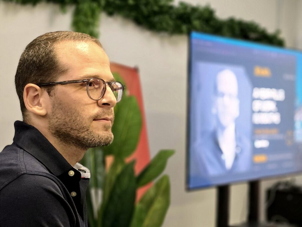 A man in glasses listening during an event, seen in profile