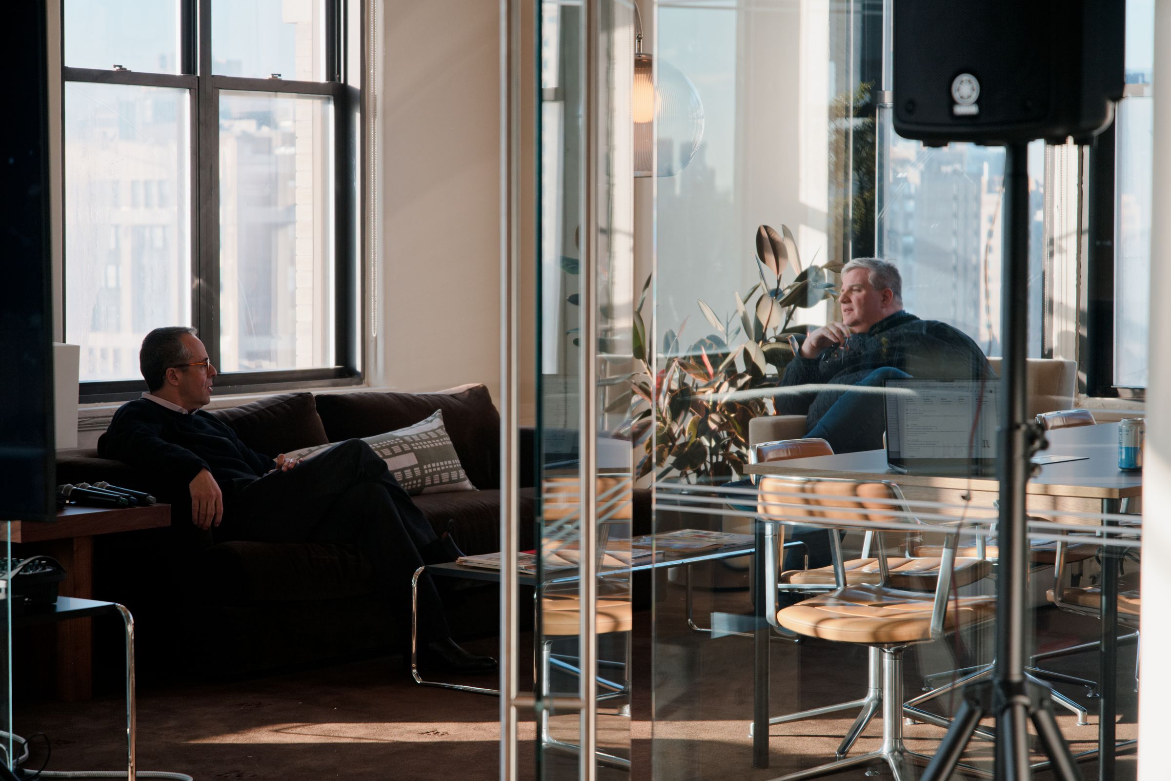 Two people in conversation in the Aboard studio, one on a sofa and one in an armchair, seen through a glass wall